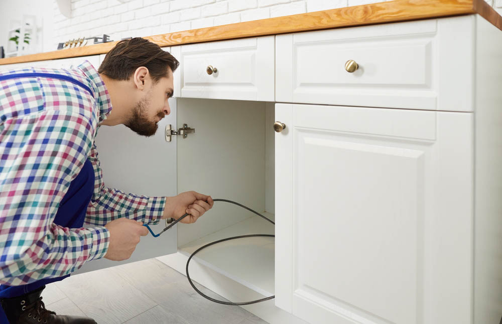 Plumber cleaning clogged drains using drain auger