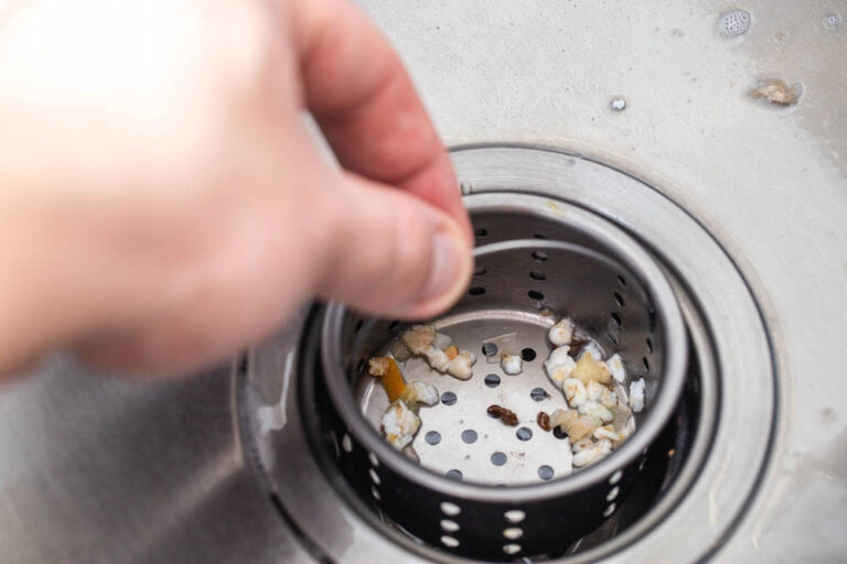 A man's hand removes a strainer from a kitchen sink drain